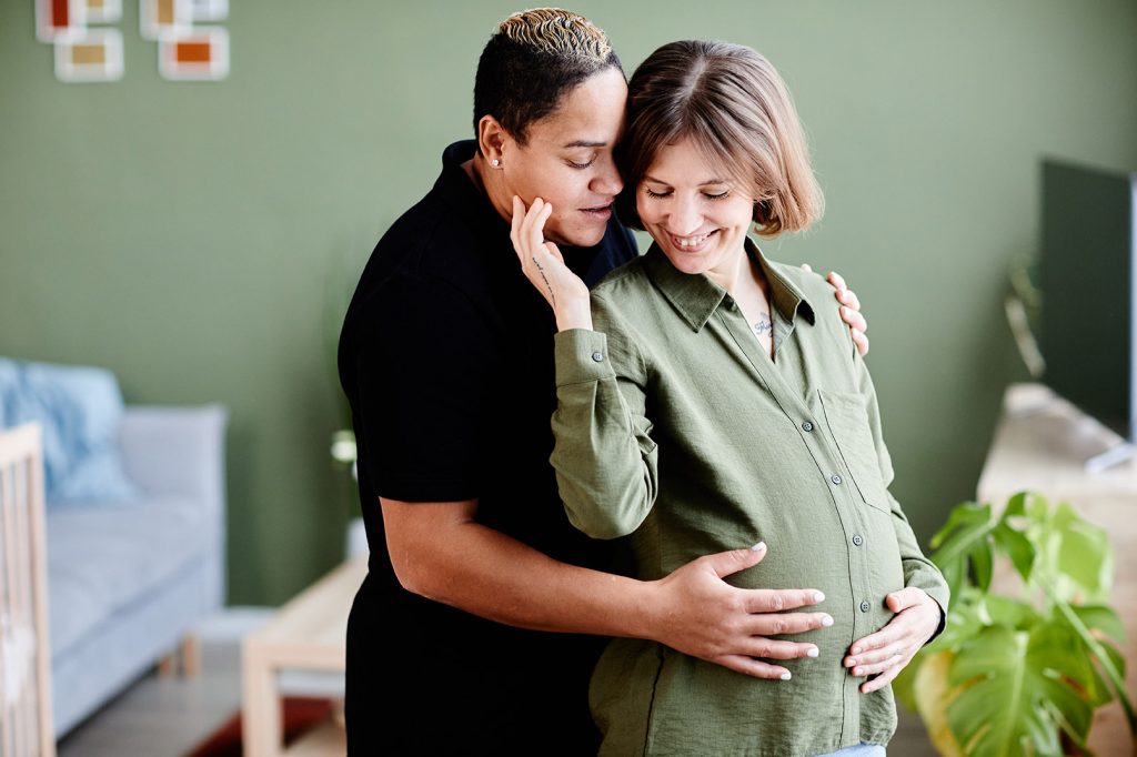 Online therapist in Texas for LGBTQ+ adults Lesbian couple with one pregnant woman lovingly caress her pregnant belly