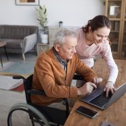 Texas senior-aged man in a wheelchair gets help from care worker logging on to online therapy session
