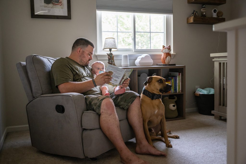 Army father sits in his PT uniform with his young baby and dog nearby